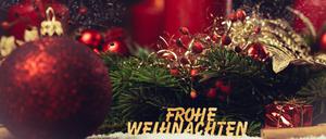 Adventskranz mit brennender Kerze und einer Holzschrift: Frohe Weihnachten.