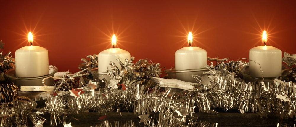 Adventsdekoration mit vier brennenden Kerzen vor rotem Hintergrund.