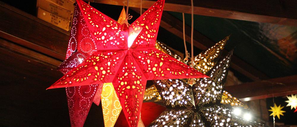 Weihnachtssterne, die beleuchtet sind, hängen unter einem Holzdach.
