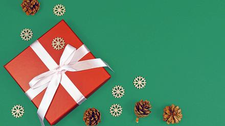 Rote Weihnachtsgeschenkbox mit Band, umgeben von saisonalen Tannenzapfen und hölzernen Schneeflockenornamenten in einer Ecke des grünen Hintergrunds mit leerem Kopierraum.