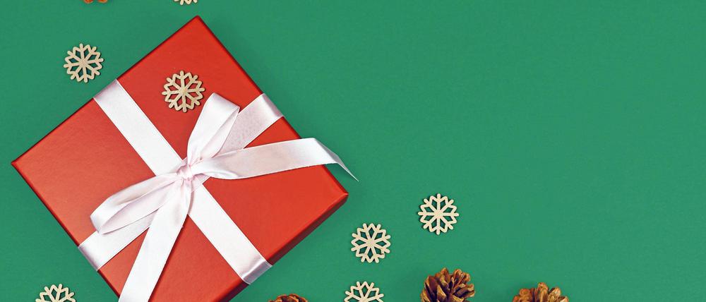 Rote Weihnachtsgeschenkbox mit Band, umgeben von saisonalen Tannenzapfen und hölzernen Schneeflockenornamenten in einer Ecke des grünen Hintergrunds mit leerem Kopierraum.