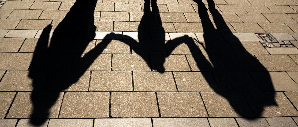 Die Schatten von zwei Erwachsenen und einem Kind fallen in den Morgenstunden auf den Asphalt.