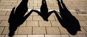 Die Schatten von zwei Erwachsenen und einem Kind fallen in den Morgenstunden auf den Asphalt. 