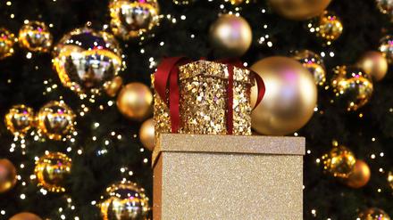 Weihnachtsgeschenke stehen gestapelt vor einem geschmückten Weihnachtsbaum.