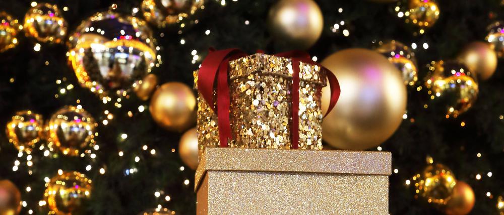 Weihnachtsgeschenke stehen gestapelt vor einem geschmückten Weihnachtsbaum.
