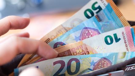 Eine Frau hält ein Portemonnaie in der Hand, in dem Geldscheine stecken. 
