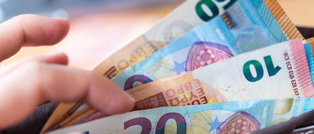 Eine Frau hält ein Portemonnaie in der Hand, in dem Geldscheine stecken.