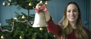 Eine lächelnde Frau zeigt eine Weihnachtsglocke.