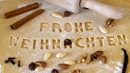 Weihnachtsplätzchen zum Ausstechen werden erstellt, der Mürbeteig auf der Küchenplatte ist mit Mehl unterlegt. Mit Buchstaben-Förmchen wurde das Wort Frohe Weihnachten ausgestochen.