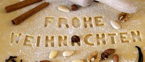 Weihnachtsplätzchen zum Ausstechen werden erstellt, der Mürbeteig auf der Küchenplatte ist mit Mehl unterlegt. Mit Buchstaben-Förmchen wurde das Wort Frohe Weihnachten ausgestochen.