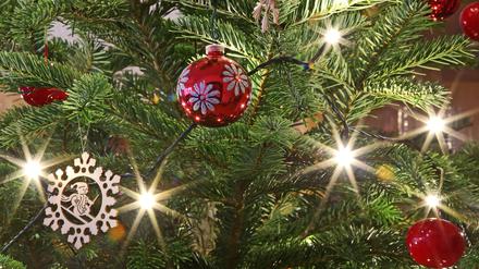 Christbaumschmuck inkklusive Christbaumkugeln hängen an einem beleuchteten Weihnachtsbaum.