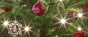 Christbaumschmuck inkklusive Christbaumkugeln hängen an einem beleuchteten Weihnachtsbaum.