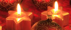 Leuchtende Weihnachtskerzen sind um Christbaumkugeln gestellt.