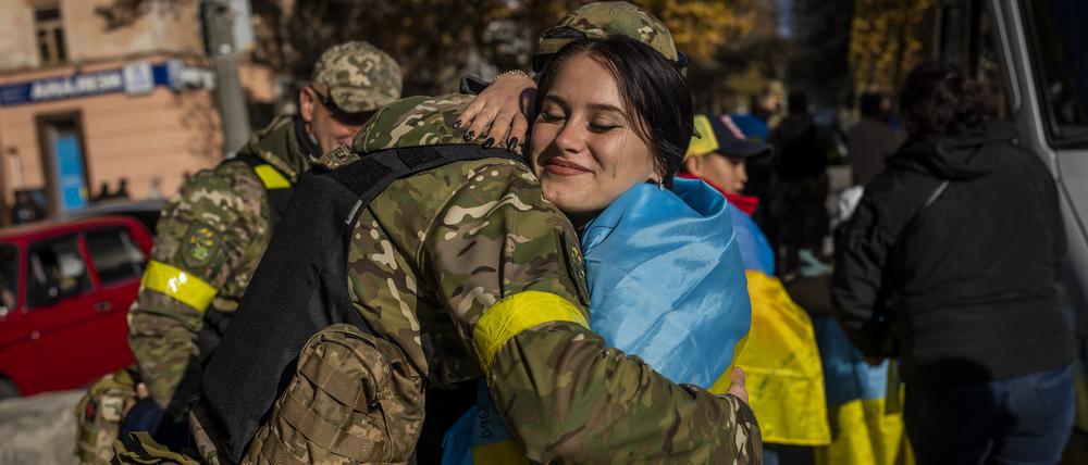 Eine Frau, die sich in eine ukrainische Fahne gewickelt hat, umarmt ein Mitglied der ukrainischen Verteidigungskräfte.