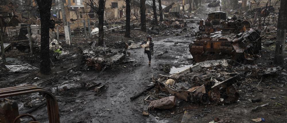 Ukraine, Butscha: Eine Frau geht auf einer Straße, die übersät ist mit zerstörten russischen Militärfahrzeugen.