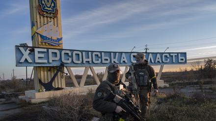 Zwei Mitglieder der ukrainischen Verteidigungskräfte stehen neben einem Schild mit der Aufschrift „Region Cherson“ am Stadtrand. 