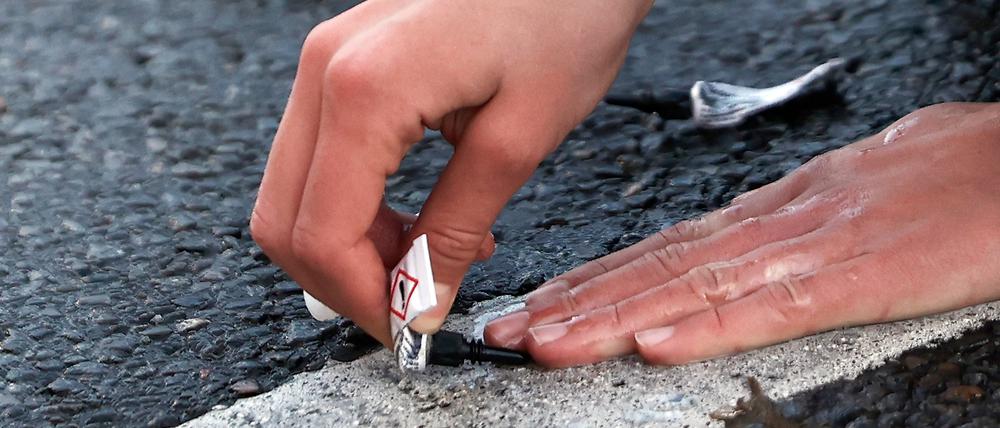 Ein Aktivist klebt seine Hand mit Sekundenkleber auf der Straße fest.