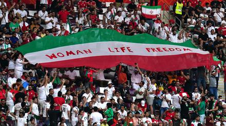 Iranische Fans halten auf der Tribüne eine Flagge mit der Aufschrift „Woman Life Freedom“ hoch.