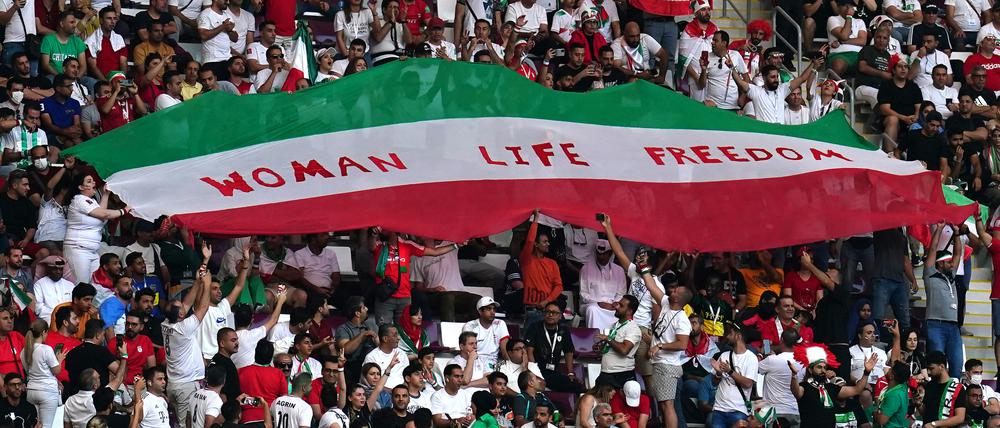 Iranische Fans halten auf der Tribüne eine Flagge mit der Aufschrift „Woman Life Freedom“ hoch.