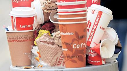 Einweg-Kaffeebecher stapeln sich auf einem vollen Mülleimer. 