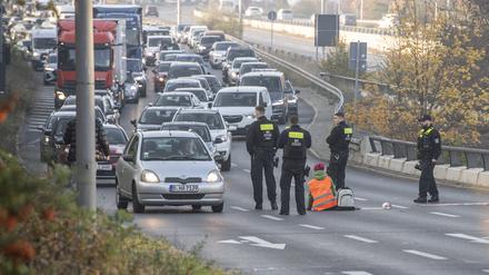 Eine Demonstrantin der Gruppe „Letzte Generation“ sitzt, umringt von Polizeibeamten, auf der Ausfahrt der Stadtautobahn am Sachsenring.