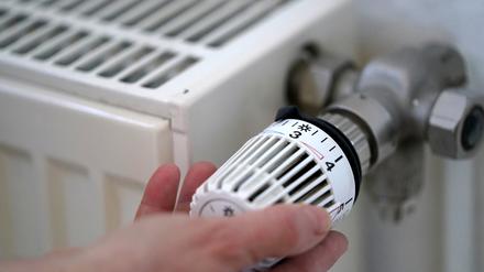 Eine Frau dreht an einem Heizungsthermostat. 