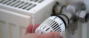 Eine Frau dreht an einem Heizungsthermostat. 