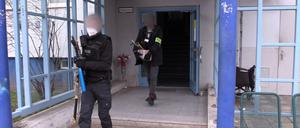 Polizisten verlassen mit beschlagnahmten Gegenständen nach einer Durchsuchung ein Haus.