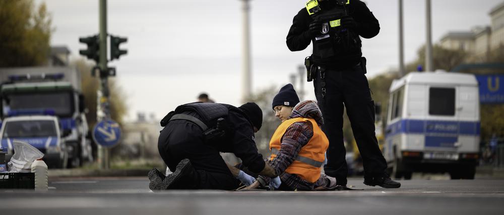 Polizisten lösen eine Aktivistin der Gruppe „Letzte Generation“ von der Kreuzung Frankfurter Tor, die sich bei einer Sitzblockade mit einer Hand am Asphalt festgeklebt hat.