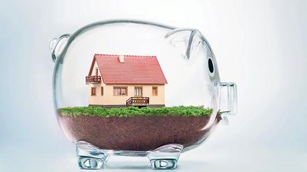 Saving to buy a house or home savings concept with model house inside transparent piggy bank. Viele Deutsche haben vor Jahren aus heutiger Sicht hochverzinste Bausparverträge abgeschlossen. Foto: POGONICI - FOTOLIA