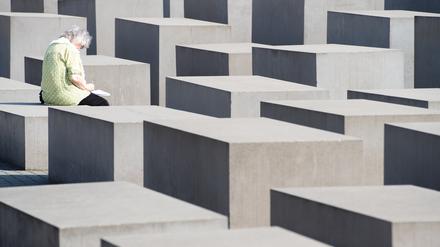 Eine Frau sitzt auf einer Stele am Denkmal für die ermordeten Juden Europas. 