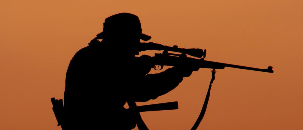 Ein Jäger sitzt bei Sonnenuntergang mit angelegtem Gewehr auf einem Hochstand unweit der brandenburgischen Ortschaft Fürstenwalde.