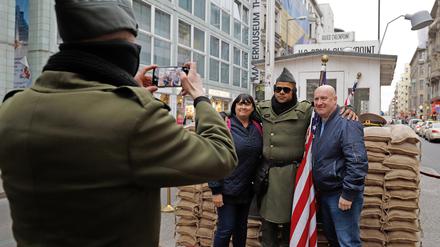 06.12.2018, Berlin: Cheryl und Collin, Touristen aus England, lassen sich am Checkpoint Charlie gemeinsam mit einem Darsteller, der eine US-Uniform trägt, fotografieren. Der Checkpoint war zu DDR-Zeiten der Übergang für Ausländer von Wets- nach Ost-Berlin. Foto: Clara Margais/dpa +++ dpa-Bildfunk +++