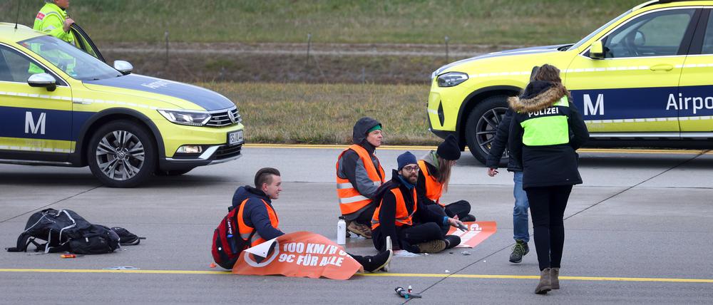 Vier Klimaaktivisten sitzen mit angeklebten Händen auf dem Zubringer einer Start-und Landebahn am Airport Franz-Josef-Strauß.