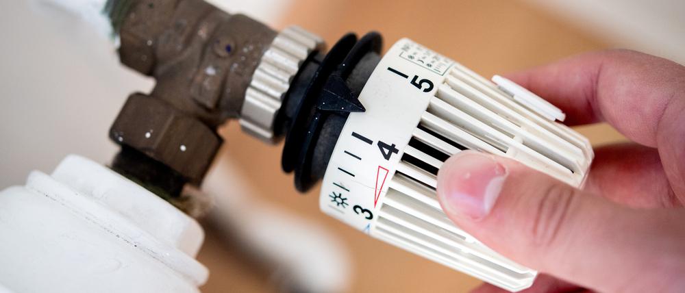 Ein Mann dreht in einer Wohnung am Thermostat einer Heizung (Symbolbild).