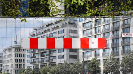 Ein rot-weiße Absperrung ist an einem Foto mit Wohn- und Geschäftshäusern in Berlin angebracht über dem die Zweige von Bäumen zu sehen sind. Das Plakat mit dem Foto dient an einem Bauzaun als Sichtschutz.