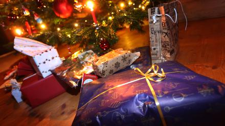 Verpackte Geschenke liegen in einem Wohnzimmer unter einem festlich geschmücktem Weihnachtsbaum. 