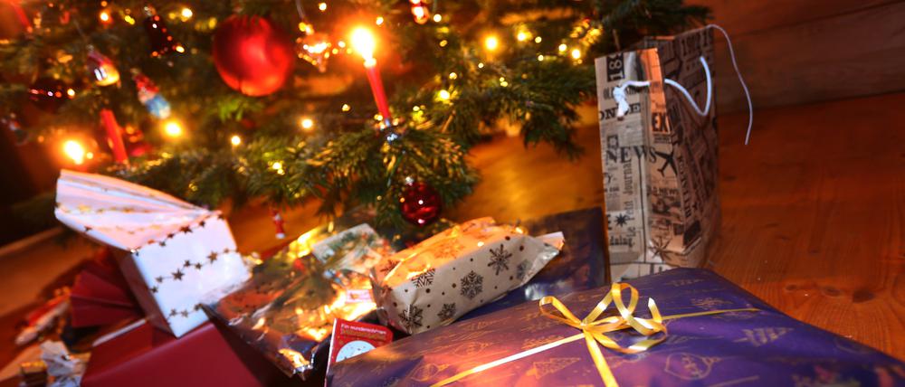 Verpackte Geschenke liegen in einem Wohnzimmer unter einem festlich geschmücktem Weihnachtsbaum. 