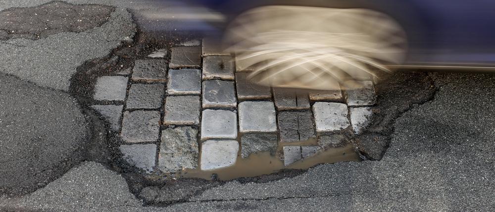 Ein Auto fährt über eine Straße mit Schlaglöchern.