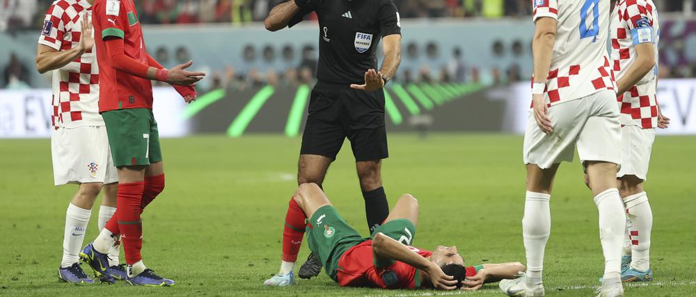 Im Chalifa International Stadion. Schiedsrichter Abdulrahman Al Jassim  gestikuliert, während Achraf Hakimi aus Marokko auf dem Rasen liegt. 
