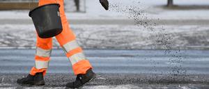 Streuen gegen das Rutschen: Ein Arbeiter in Schutzkleidung ist auf einem Gehweg mit Streuarbeiten beschäftigt.