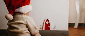 Ein Kind mit Weihnachtsmannmütze sitzt vor einer kleinen Wichteltür in der Wand.