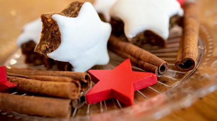 Mehrere Zimtsterne liegen neben Zimtstangen und roten Holzsternen auf einem Teller.