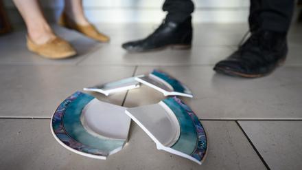 Ein Mann und eine Frau stehen hinter einem zerbrochenen Teller in einer Küche.