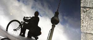 Radfahrerin spiegelt sich in Pfütze mit Fernsehturm am Alexanderplatz.