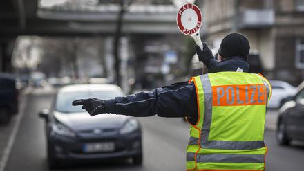 Ein Polizeibeamter stoppt ein Auto mit Hilfe einer Polizeikelle im Rahmen einer Verkehrskontrolle (Symbolbild).