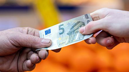 ARCHIV - 29.01.2022, Niedersachsen, Hannover: Ein Kunde bezahlt seinen Einkauf an einem Stand auf einem Wochenmarkt mit einem Fünf-Euro-Schein (gestellte Szene). Bezahlen ohne Scheine und Münzen gewinnt für Verbraucher im Euroraum nach Einschätzung der Europäischen Zentralbank (EZB) zunehmend an Bedeutung. (zu dpa «EZB-Studie: Bargeld verliert beim Bezahlen an Bedeutung») Foto: Moritz Frankenberg/dpa +++ dpa-Bildfunk +++