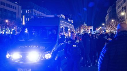 Ein Polizeiauto fährt vor dem Brandenburger Tor mit Blaulicht durch die Menschenmenge. 