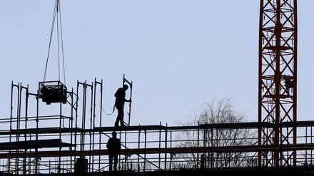 Handwerker arbeiten am Neubau eines Mehrfamilienhauses an einem Baugerüst. 