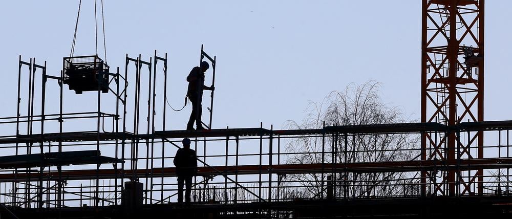 Handwerker arbeiten am Neubau eines Mehrfamilienhauses an einem Baugerüst.